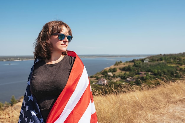 Retrato al aire libre de una mujer con bandera americana en la naturaleza en un día soleado