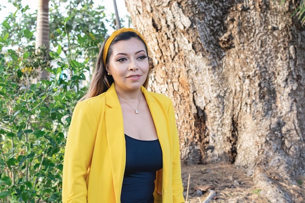 Retrato al aire libre de mujer con chaqueta amarilla Retrato de joven mexicana en un jardín al atardecer