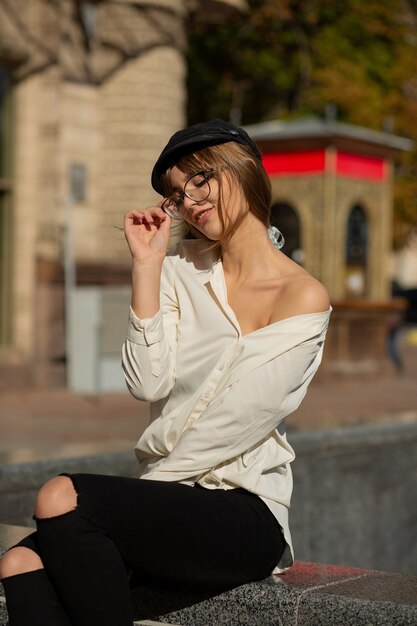 Retrato al aire libre de la mujer morena de moda lleva elegante gorra, gafas y blusa posando en la ciudad