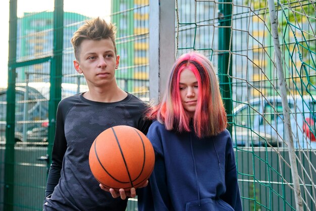 Retrato al aire libre de pareja adolescente novio y novia en cancha de baloncesto con pelota. Deportes activos estilo de vida saludable de los adolescentes en la ciudad