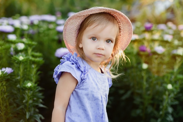 Foto retrato al aire libre pequeña muchacha encantadora del niño con las flores en el jardín hermoso. niño al aire libre en la naturaleza