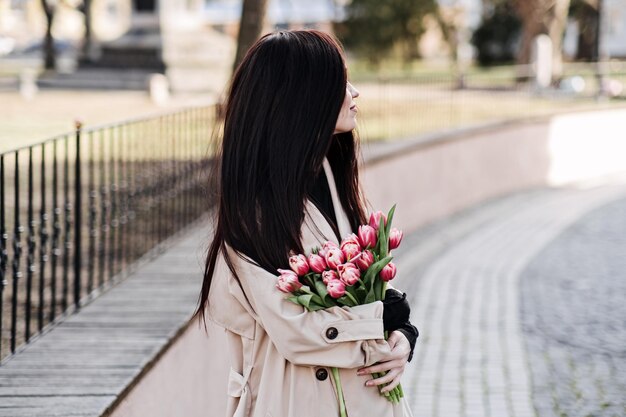 Retrato al aire libre de primavera de mujer feliz con un ramo de tulipanes y café para ir a la calle de la ciudad de primavera mujer joven feliz sosteniendo un bouquet de flores rosas
