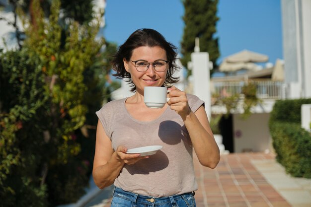 Retrato al aire libre de verano de mujer sonriente madura caminando con una taza de café