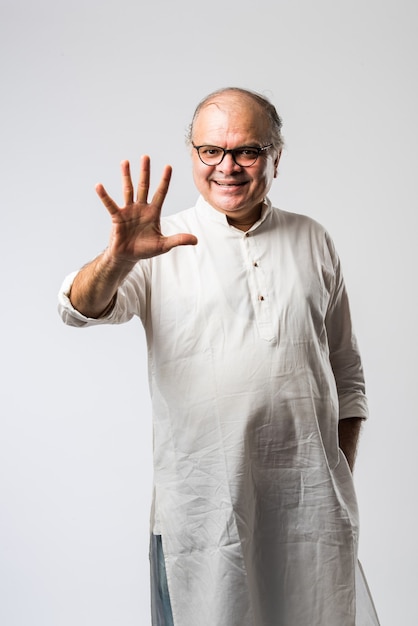 Retrato de alegre anciano jubilado indio viste kurta blanco, señalando o presentando o en pose de manos dobladas