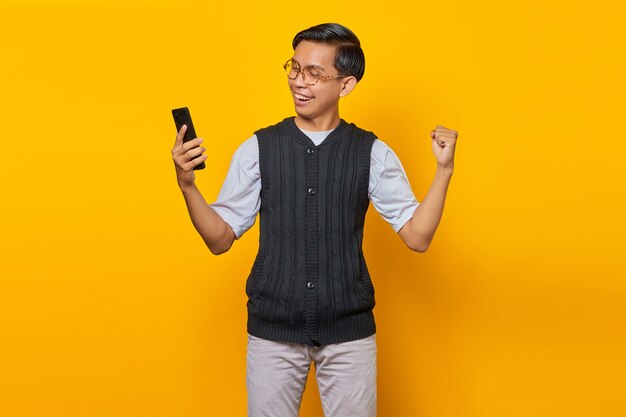 Retrato de alegre apuesto hombre asiático con smartphone y regocijo celebrando la suerte