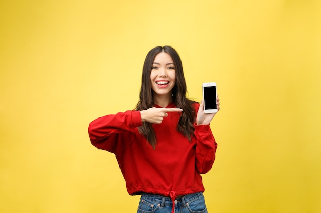 Retrato de una alegre chica casual sosteniendo teléfono móvil y dedo acusador