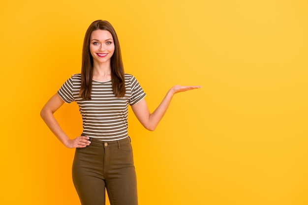 Retrato de alegre chica positiva promotora mantenga la mano seleccione sugerir promoción actual anuncios usan ropa de buen aspecto aislado sobre paredes de colores vivos