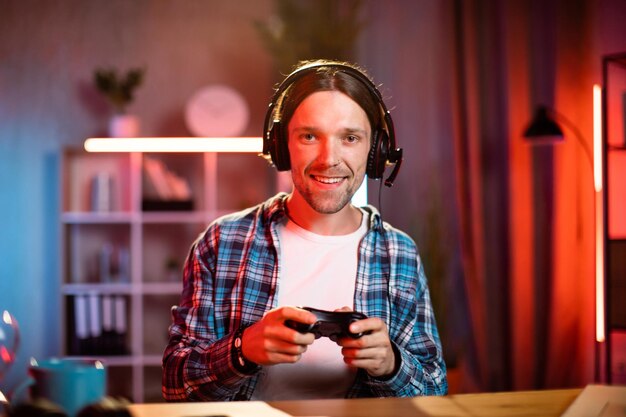 Retrato de un alegre chico caucásico con auriculares usando una consola remota para jugar videojuegos en casa