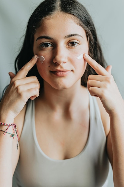 Retrato alegre e engraçado de uma jovem adulta com creme de loção nas bochechas Skincare rosto beleza e mulher com creme para acne dermatologia e brilho em um fundo de estúdio