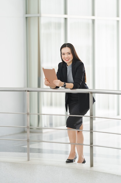 Retrato de una alegre empresaria asiática confiada en un traje de negocios de pie whie usando una tableta digital en el edificio del negocio. Foto de archivo de negocios