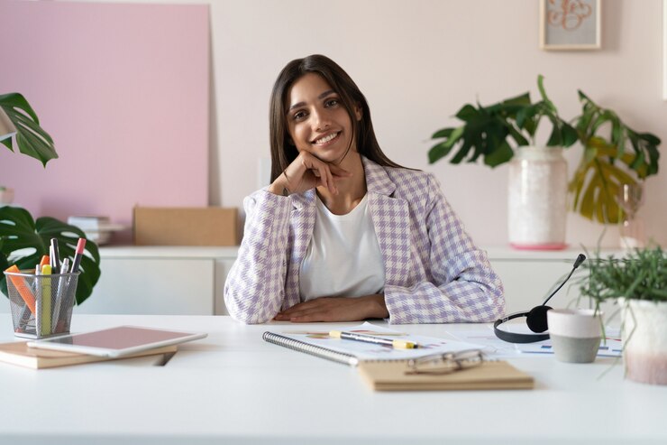 Foto retrato de una alegre empresaria india de raza mixta sentado en la mesa en la oficina y mirando a la cámara.