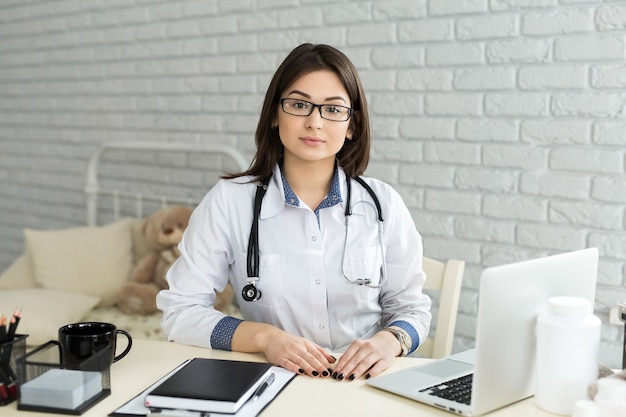 Retrato de alegre feliz doctora sentada en su lugar de trabajo