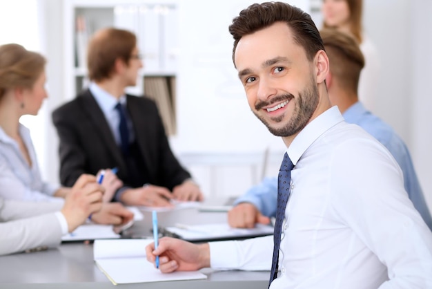 Retrato de un alegre hombre de negocios sonriente contra un grupo de empresarios en una reunión.