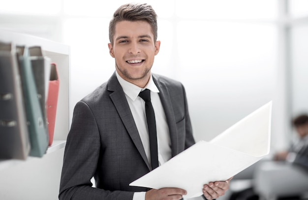 Foto retrato de un alegre hombre de negocios vestido con elegante ropa formal sosteniendo una carpeta con documentos financieros en la mano y sonriendo a la cámara