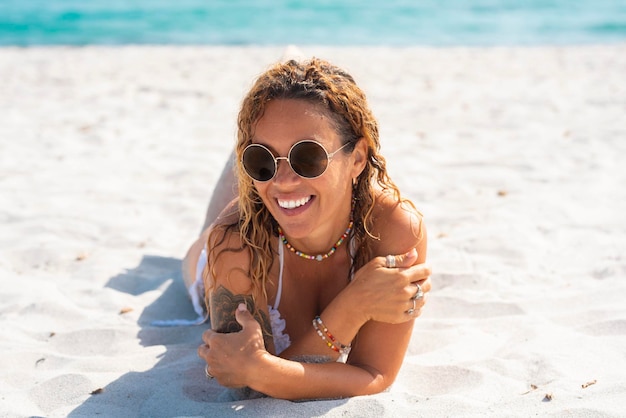 Retrato de una alegre joven adulta tendida en la playa sobre arena blanca Vacaciones de verano tropical Las mujeres relajadas sonríen y disfrutan del sol Agua de mar azul en el fondo Ocio de viajes