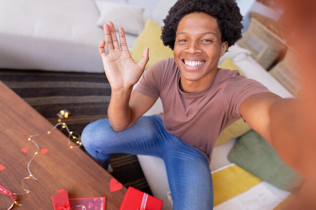 Retrato de un alegre joven afroamericano agitando la mano por videollamada mientras estaba sentado en casa