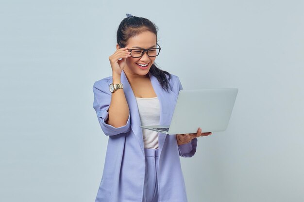 Retrato de una alegre joven asiática sosteniendo una laptop y quitándose las gafas aisladas de fondo blanco