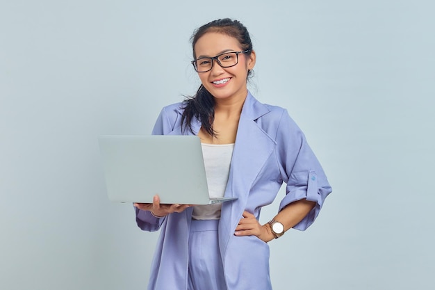 Retrato de una alegre joven asiática usando una laptop y mirando una cámara aislada de fondo blanco