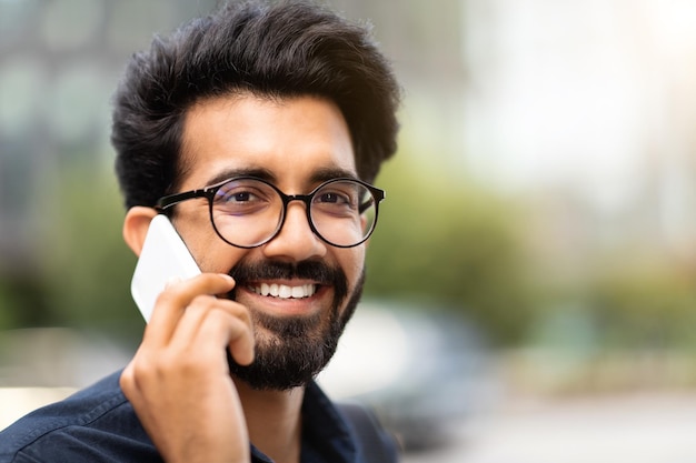 Retrato de alegre joven empresario indio hablando por teléfono