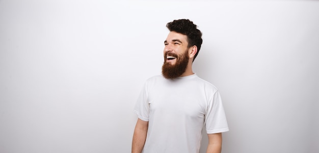 Retrato de alegre joven sonriente con barba en camiseta blanca mirando a otro lado copyspace