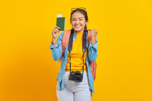 Retrato de un alegre joven viajero asiático que muestra el billete de la tarjeta de embarque del pasaporte y celebra la buena suerte aislado en un fondo amarillo. Pasajeros que viajen los fines de semana. Concepto de viaje de vuelo aéreo