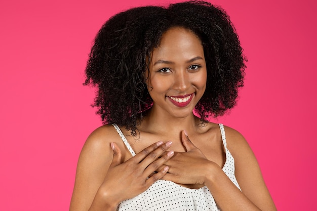 Retrato de alegre linda joven afroamericana rizada puso las manos en su pecho agradecida