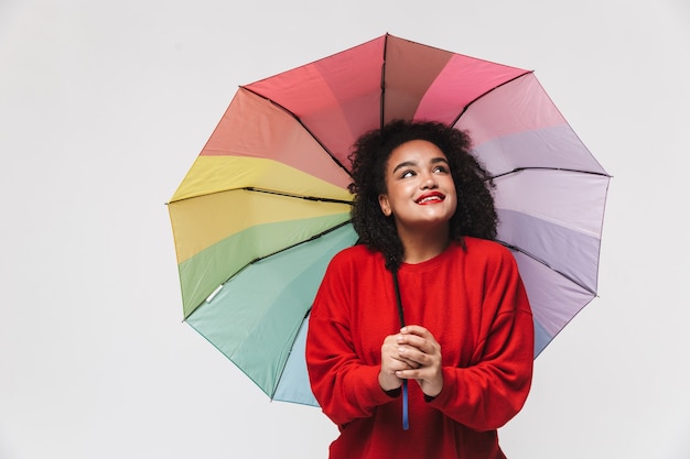 Retrato de una alegre mujer africana que se encuentran aisladas sobre fondo blanco, sosteniendo coloridos paraguas