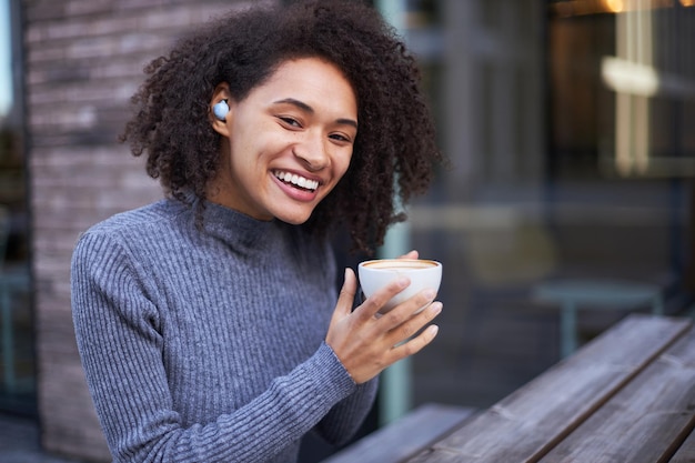 Retrato de una alegre mujer afroamericana sosteniendo una taza de bebida caliente y sonriendo mirando a la cámara