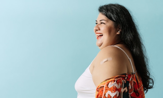 Foto retrato alegre mujer latinoamericana de talla grande mirando a otro lado con una venda en el brazo después de la vacuna.