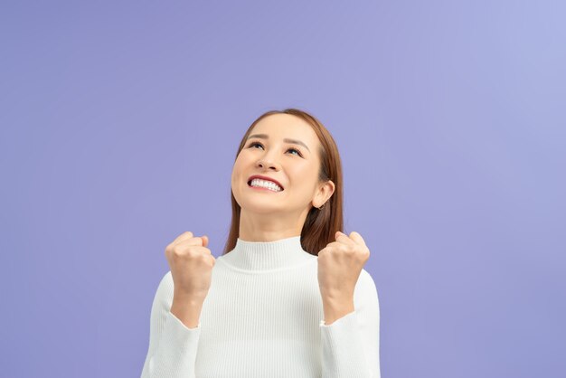 Retrato de una alegre niña asiática feliz celebrando el éxito mientras baila aislado sobre la pared violeta