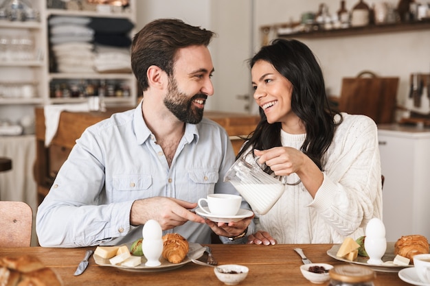 Retrato de alegre pareja europea hombre y mujer tomando café mientras desayuna en la cocina de casa