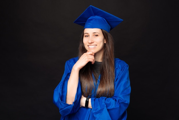 Retrato de alegre sonriente joven estudiante mujer vistiendo soltero y sombrero de graduación sobre fondo negro