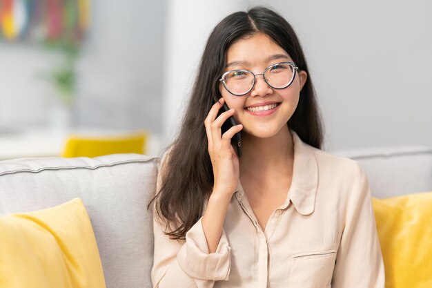 Retrato de una alegre y sonriente jovencita positiva sentada en un sillón de sofá hermoso cabello oscuro