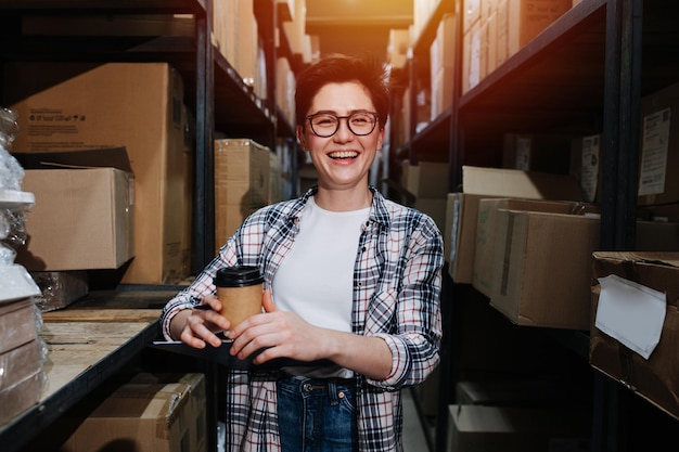 Retrato de una alegre trabajadora de almacén parada entre estantes