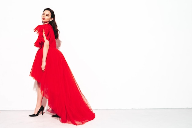 Retrato de alta moda de una joven y bella mujer morena con un bonito vestido rojo de noche esponjoso Modelo de moda sexy posando en el estudio Mujer de moda aislada en blanco