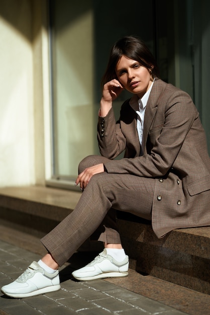 Retrato de alta moda de mujer elegante joven en traje marrón a pie en la calle. disfruta las luces de verano. Foto de moda