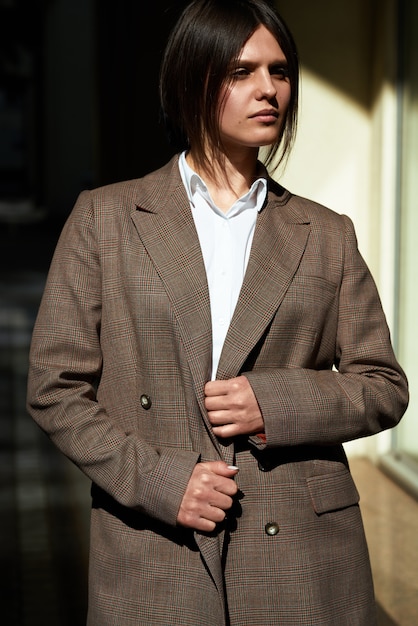 Retrato de alta moda de mujer elegante joven en traje marrón a pie en la calle. disfruta las luces de verano. Foto de moda