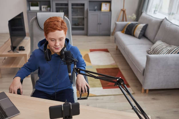 Retrato de alto ángulo de un adolescente pelirrojo hablando con el micrófono y grabando video mientras transmite en línea, espacio de copia
