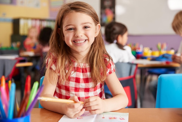 Retrato de una alumna de escuela primaria femenina sonriente trabajando en un escritorio