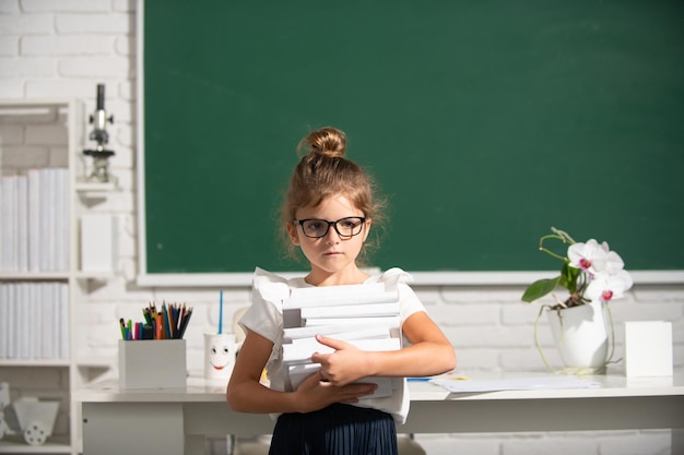 Retrato de una alumna seria de la escuela primaria estudia una colegiala nerd con gafas con libros en bla