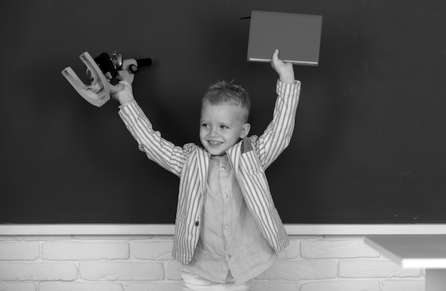 Retrato de un alumno gracioso de la escuela primaria estudiando en el aula de la escuela un niño pequeño con un microscopio