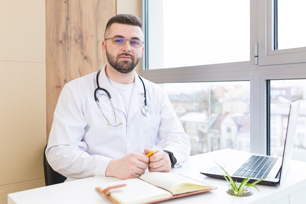 Retrato de un amable médico en uniforme con portátil