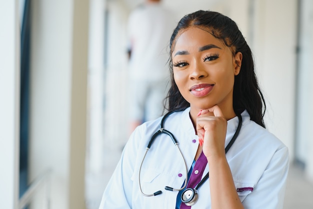 Retrato de amable, sonriente profesional de la salud femenina confiada con bata de laboratorio, brazos cruzados sosteniendo gafas. Fondo aislado de la clínica del hospital.