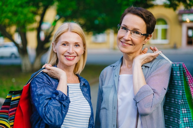 Retrato de amigas felices de pie afuera sosteniendo bolsas de compras sonriendo