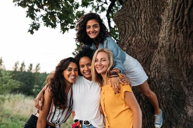 Retrato de amigas sonrientes cerca del tronco del árbol