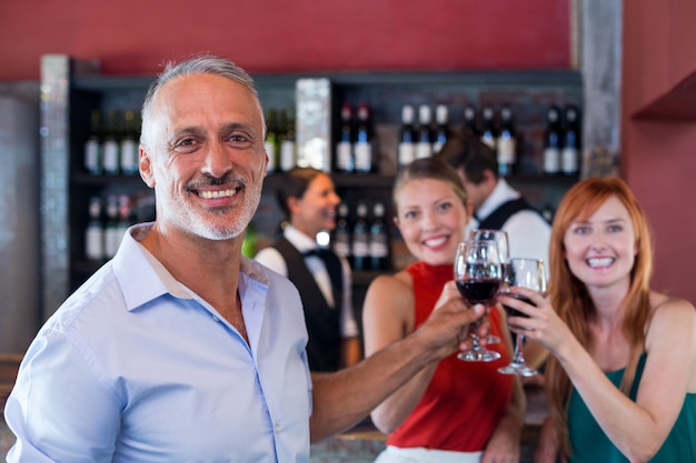 Retrato de amigos brindando con una copa de vino tinto en un bar.