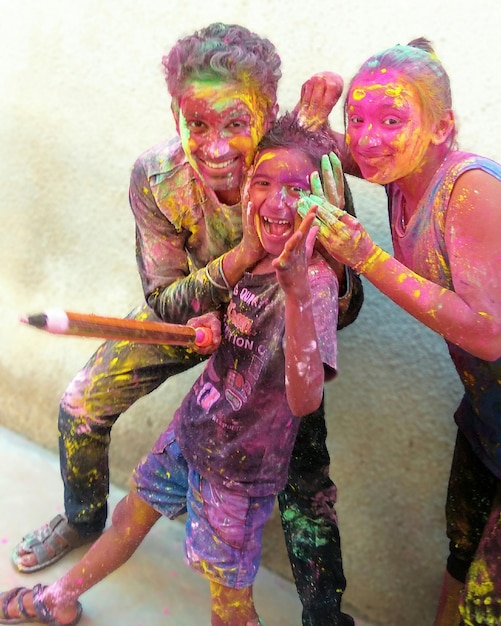 Foto retrato de amigos jugando holi mientras están de pie contra la pared