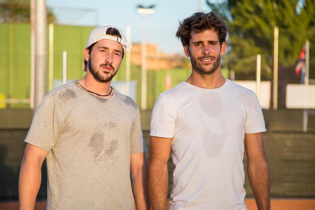 Foto retrato de amigos masculinos de pie en la cancha de tenis durante la puesta de sol