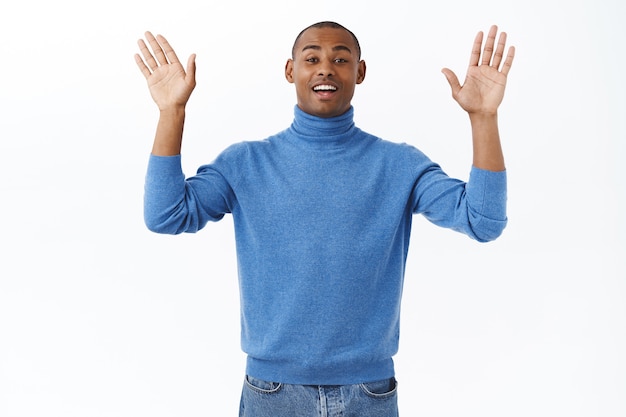 Retrato de amistoso apuesto hombre afroamericano agitando las manos levantadas, diciendo adiós o hola