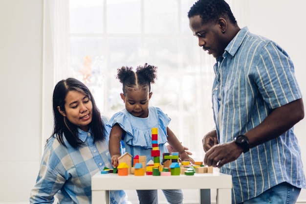 Retrato de amor feliz familia negra padre afroamericano y madre con niñita actividad sonriente aprender y entrenar el cerebro jugar con juguetes construir bloques de madera juego de educación en casa
